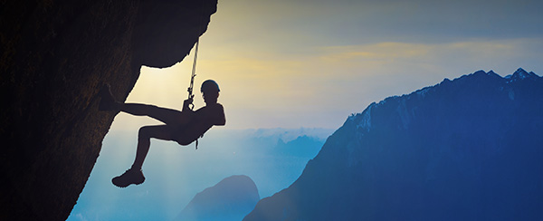 A man hanging from a rope on top of a mountain.